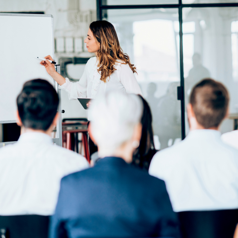 Frau zeichnet an Whiteboard vor Publikum