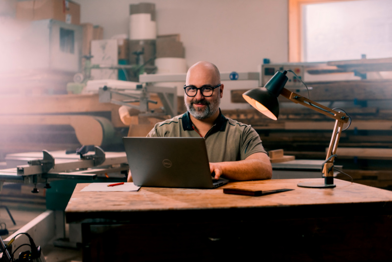 Handwerker in Werkstatt an Schreibtisch mit Laptop